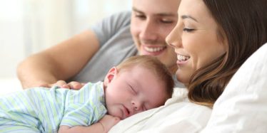 Happy parents watching their baby sleeping on a bed at home